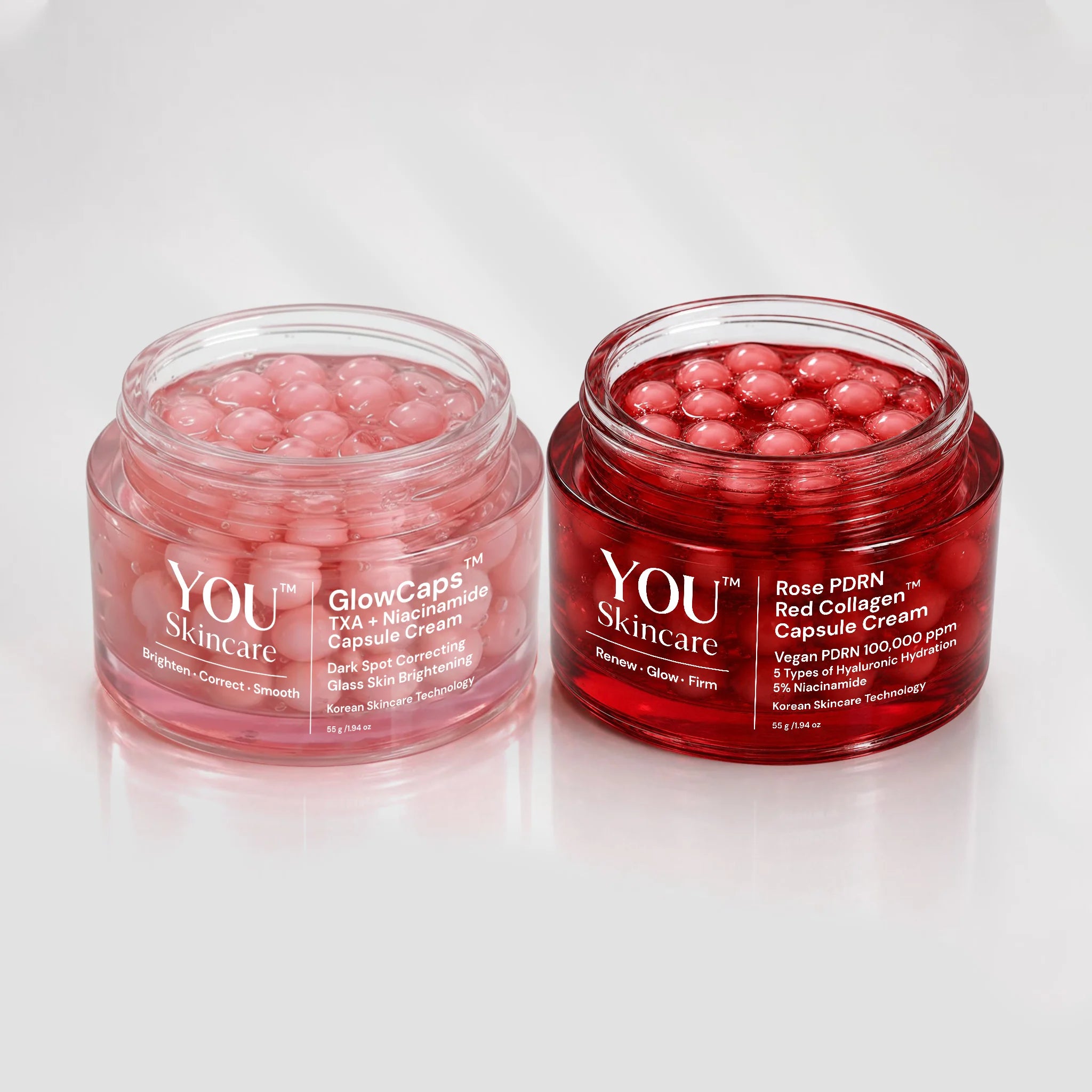Two clear cosmetic jars filled with pink/red capsules on a white reflective background. The left jar is labeled YOU Skincare GlowCaps and the right jar is labeled YOU Skincare Rose DORN Red Collagen Capsule Cream.