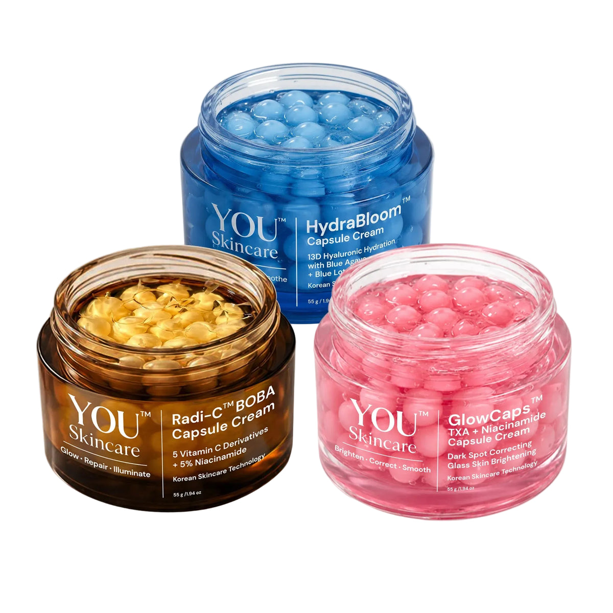 Three open cosmetic capsule cream jars from YOU Skincare on a light gray background: a brown Radi-C Capsule Cream jar with yellow capsules, a blue HydraBloom Capsule Cream jar with blue capsules, and a pink GlowCap5 Capsule Cream jar with pink capsules.