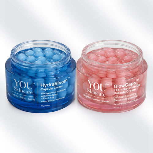 Two open cosmetic jars on a light gray background: a blue jar labeled YOU Skincare HydraBloom Capsule Cream and a pink jar labeled YOU Skincare GlowCaps TXA + Microneedle Capsule Cream, each filled with round gel capsules.