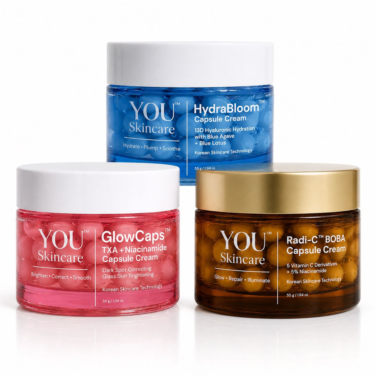 Three cosmetic cream jars from YOU Skincare arranged on a white background: a blue HydraBloom Capsule Cream jar in the back, a pink GlowCaps TXA + Niacinamide Capsule Cream jar in the front left, and a brown Radi-C BOBA Capsule Cream jar with a gold lid in the front right.