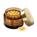 A jar of YOU Skincare Radi-C™ BOBA Capsule Cream with its gold lid leaning against it, showing golden yellow capsules inside the amber glass jar, on a white background.